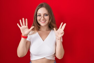 Young caucasian woman standing over red background showing and pointing up with fingers number nine while smiling confident and happy.