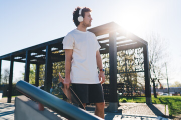 Male skater standing with skateboard listening to music in headphones © BullRun