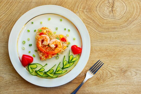 Naklejki Heart shaped shrimp fried rice served with heart shaped cucumbers and tomatoes on plate with wooden background.Creative art food idea for Valentine or Mother day.Top view.Copy space