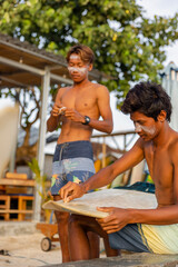 Fototapeta Surfers cleaning surfboard and applying sun lotion on face at beach obraz