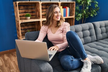 Fototapeta na wymiar Young woman using laptop sitting on sofa at home