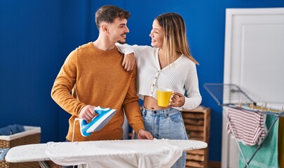 Young man and woman couple ironing clothes drinking coffee at laundry room