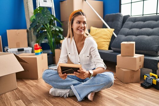 Young hispanic woman looking photo sitting on floor at new home