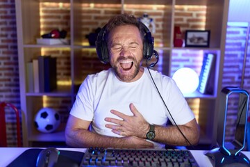Middle age man with beard playing video games wearing headphones smiling and laughing hard out loud...