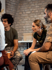 Female soldier talking with diverse group of veterans during PTSD support group.