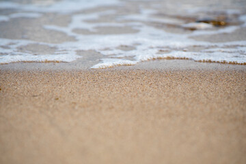 Close-up of a sandy beach with a transparent wave. Sea coast on a summer day.