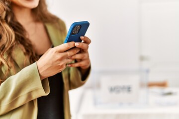 Young beautiful hispanic woman voter using smartphone at electoral college