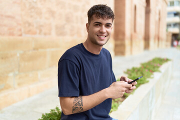 Obraz premium Young hispanic man smiling confident using smartphone at street