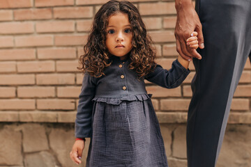 Adorable little girl looking at the camera while holding her father's hand