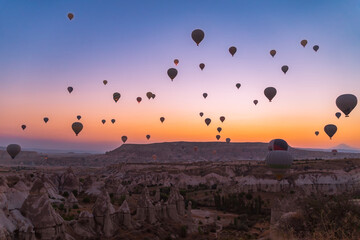 Many beautiful colorful balloons in the sky at a fabulous sunrise over the rocks, mountains in Goreme
