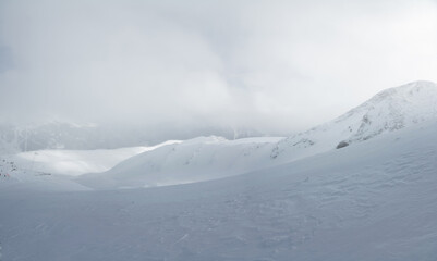 Fototapeta na wymiar Mountain landscape of a snowy valley without people, sunlight breaks through a foggy cloud