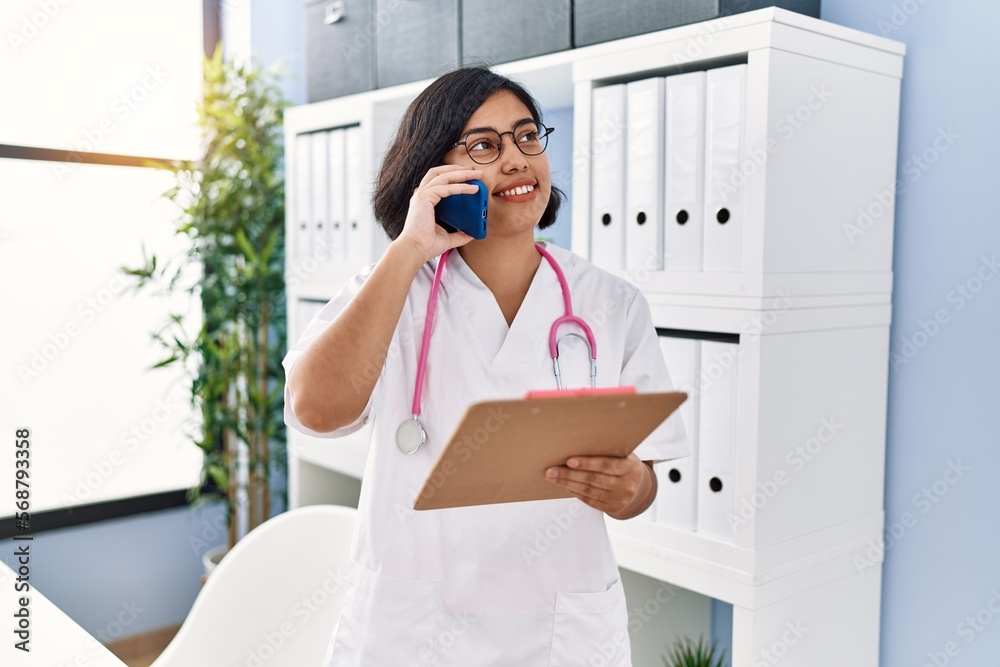 Sticker young latin woman wearing doctor uniform talking on the smartphone at clinic