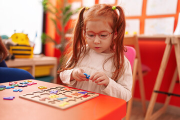 Fototapeta premium Adorable redhead girl playing with maths puzzle game sitting on table at kindergarten