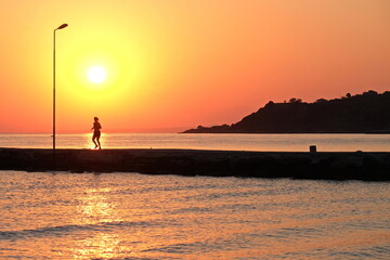 Jogger training at sunset on pier with sun and mountains in the background