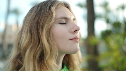 Obraz premium Young blonde woman breathing with closed eyes at park