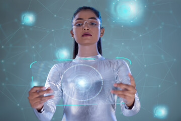 A woman wearing silver futuristic  clothes holding virtual tablet, with virtual icons in the background. A future technology concept