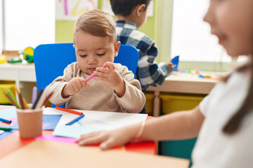 Adorable blond toddler preschool student sitting on table drawing on paper at kindergarten