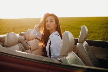 young beautiful woman in a white shirt sitting in a red car cabriolet with a white interior. red...