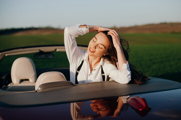 happy young beautiful woman in a white shirt sitting in a red car cabriolet with a white interior....