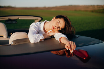 young beautiful woman in a white shirt sitting in a red car cabriolet with a white interior. red...