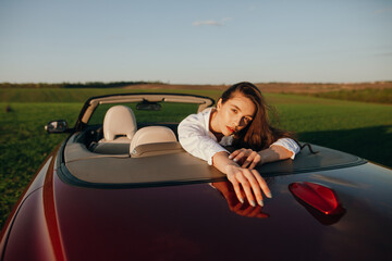 young beautiful woman in a white shirt sitting in a red car cabriolet with a white interior. red...