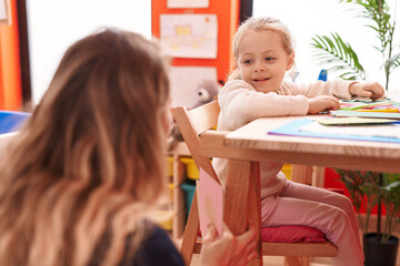 Teacher and toddler sitting on table having lesson at kindergarten