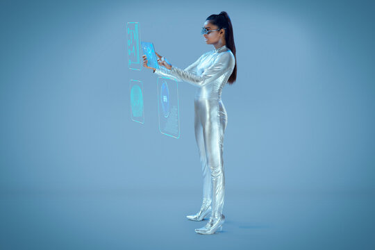 A model dressed as a robot wearing silver, futuristic  clothes holding a virtual  tablet, with virtual icons . A future technology concept