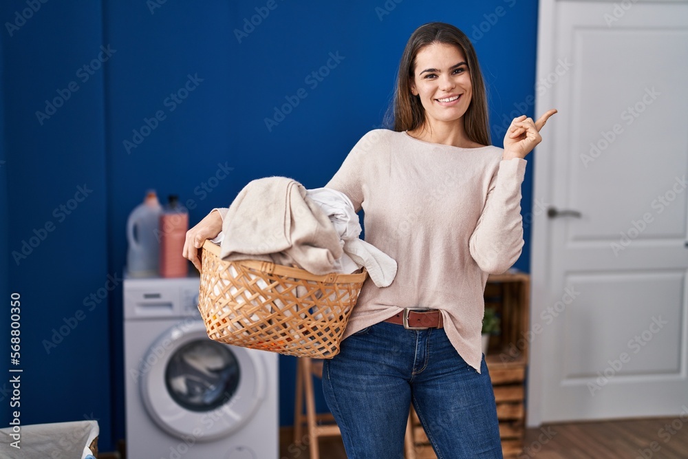 Sticker Beautiful woman holding laundry basket smiling happy pointing with hand and finger to the side