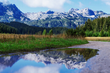 Fototapeta na wymiar Panoramic view of the mountain peaks on a sunny summer day. The mountain range is reflected in puddles. Blue sky with clouds.