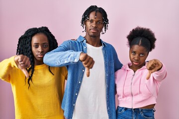 Group of three young black people standing together over pink background looking unhappy and angry...