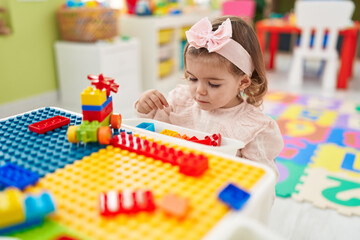 Adorable blonde toddler playing with construction blocks sitting on table at kindergarten