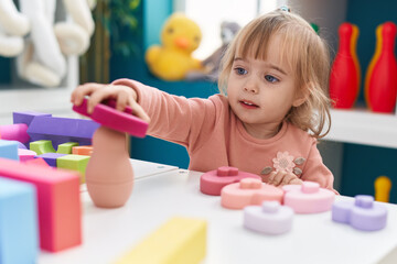 Adorable blonde girl playing with construction blocks sitting on table at kindergarten