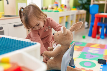 Adorable blonde girl playing with rabbit doll at kindergarten