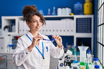 Young hispanic woman scientist smiling confident holding security glasses at laboratory