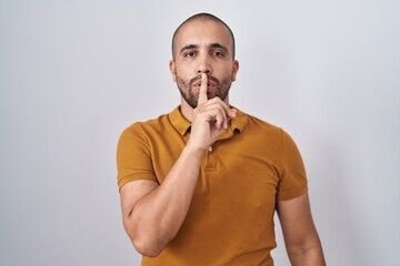 Hispanic man with beard standing over white background asking to be quiet with finger on lips. silence and secret concept.