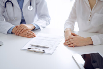 Doctor and patient discussing current health questions while sitting near of each other and using clipboard at the table in clinic, just hands closeup. Medicine concept