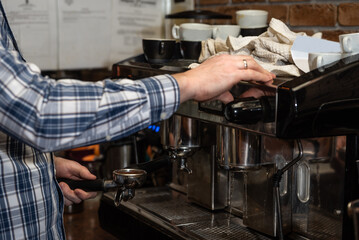 Hands of young bartender in uniform making espresso coffee on coffee machine doing the whole process
