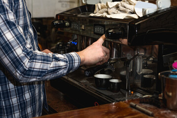 Hands of young bartender in uniform making espresso coffee on coffee machine doing the whole process