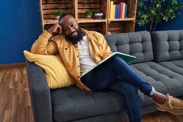 Young african american man reading book sitting on sofa at home