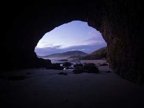 Looking out of a rock sea cave on idyllic black sand Te Henga Bethells beach during sunset in West Auckland New Zealand