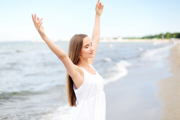 Fototapeta na wymiar Happy smiling woman in free happiness bliss on ocean beach standing with raising hands. Portrait of a multicultural female model in white summer dress enjoying nature during travel holidays vacation 