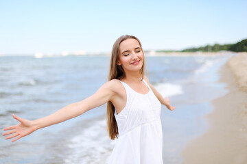 Happy smiling woman in free happiness bliss on ocean beach standing with open hands. Portrait of a multicultural female model in white summer dress enjoying nature during travel holidays 