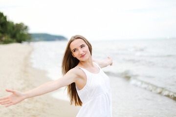 Happy smiling woman in free happiness bliss on ocean beach standing with open hands. Portrait of a multicultural female model in white summer dress enjoying nature during travel holidays vacation 