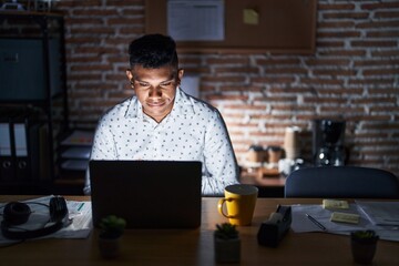 Young hispanic man working at the office at night with hand on stomach because nausea, painful disease feeling unwell. ache concept.