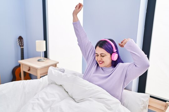 Young beautiful plus size woman dancing and listening to music sitting on bed at bedroom
