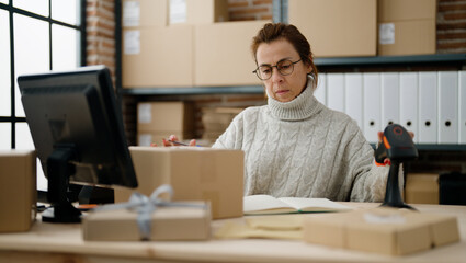 Middle age hispanic woman ecommerce business worker scanning package using barcode reader at storehouse office