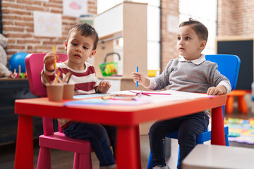 Two kids preschool students sitting on table drawing on paper at kindergarten
