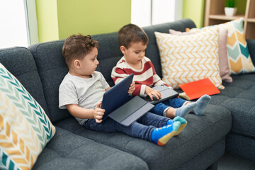 Two kids watching video on touchpad sitting on sofa at home