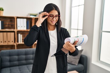 Young latin woman psychologist holding clipboard standing at clinic