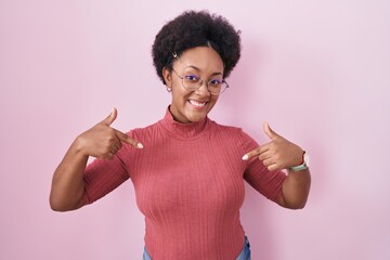 Beautiful african woman with curly hair standing over pink background looking confident with smile...